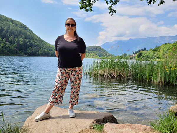 Ayleen steht vor einem See in sommerlicher Kleidung mit schwarzer Sonnenbrille